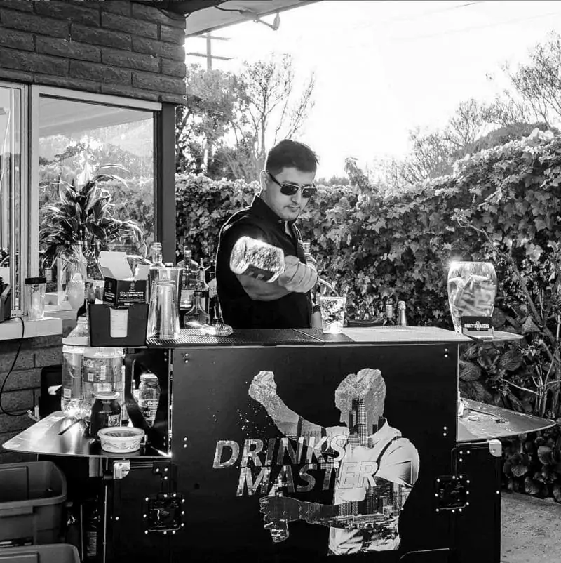 A bartender pouring liquor behind a black bar | Full bar set up