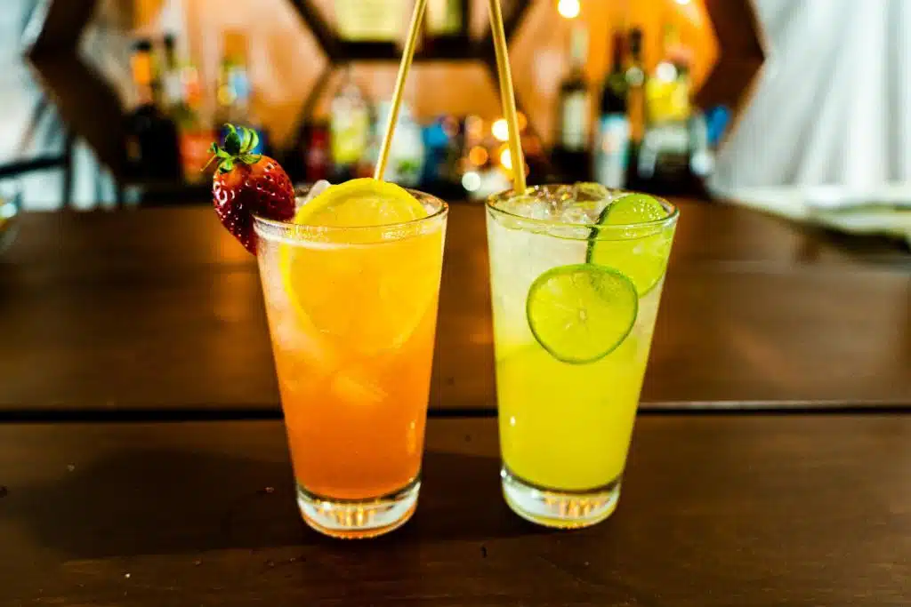 Two cocktails on the table. Inside of those cocktails some juice, liquor, lime, lemon, strawberry and ice.