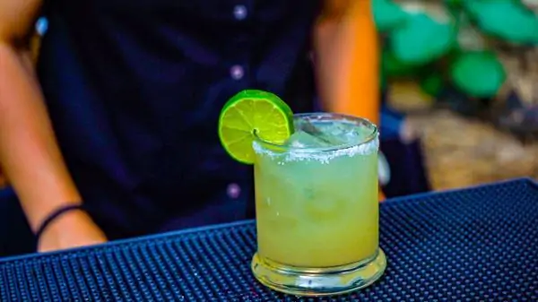 a glass with mix drink in it on a table. It has lime garnish on it. A margarita cocktail